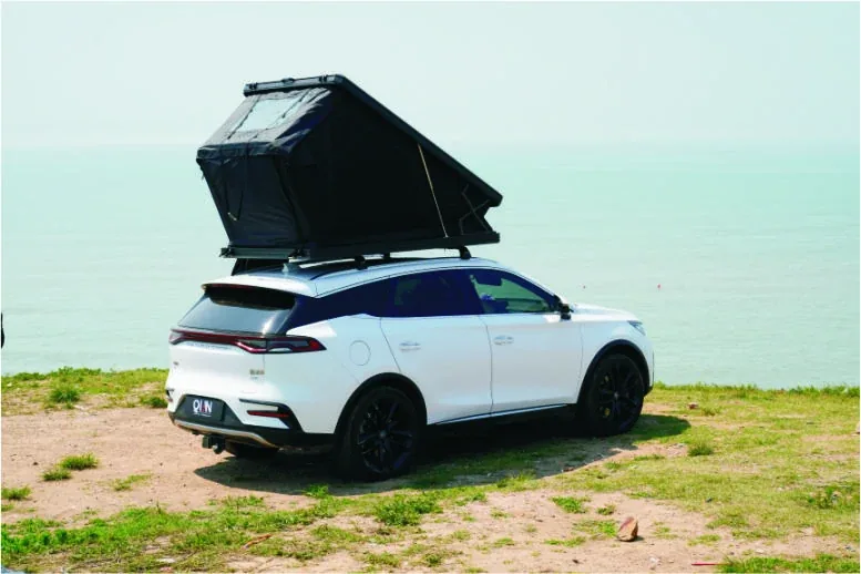 SUV fitted with a TUYU hard-shell roof-top tent on a coastal road